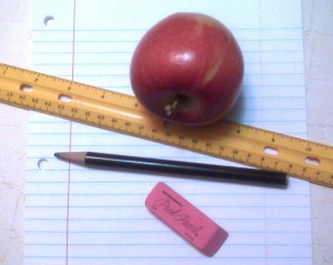 School supplies, including a ruler, pencil, eraser, notebook paper, and an apple.