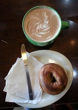 Mocha latte' in a mug and cinnamon raisin bagel on a plate with a knife and napkins at Blue Steele Coffee Company.